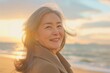 © GlooStock - Portrait of a joyful older woman with gray hair, smiling warmly as she enjoys a serene moment on the beach at sunset. The soft, golden light enhances her natural beauty and reflects a sense of peace