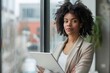 © Raool - Business woman holding a tablet and standing next to a window, Generative AI