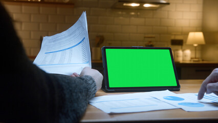 Two men working with tablet computer with green mock up screen on table in the kitchen. Co-workers working with papers, remote work, home office concept	