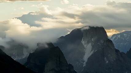 Sticker - A breathtaking sight of jagged mountain peaks adorned with fluffy white clouds as if wearing a fluffy white hat.