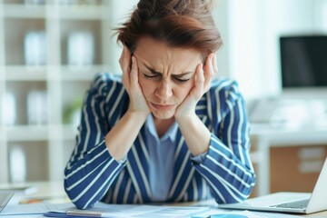 A businesswoman in a striped blazer sitting at her desk, looking stressed and overwhelmed, with her head in her hands.