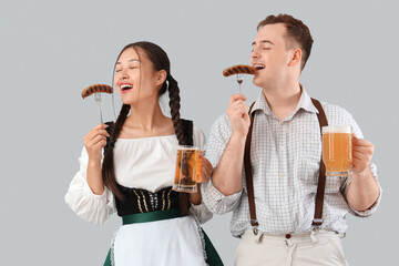 Canvas Print - Young happy couple in traditional German clothes with sausages and mugs of beer on grey background