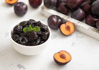 Wall Mural - Sweet prunes in glass bowl with ripe plums in wooden box on light kitchen background.