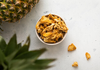 Wall Mural - Dried pineapple slices chips in glass bowl on light background with ripe pineapple fruit.Top view.