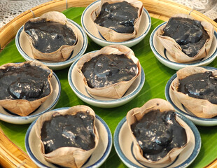 Charcoal pandanus pudding with coconut cream on dried banana leaf.