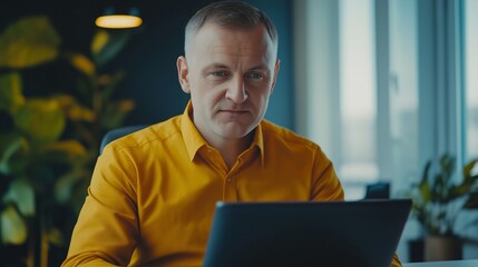 Poster - A man in a yellow shirt is sitting at a desk with a laptop in front of him. He is focused on his work, possibly typing or browsing the internet. The room has a modern and professional feel