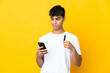 © luismolinero - Young man over isolated yellow background buying with the mobile with a credit card while thinking