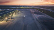 © VK Studio - Aerial view of an airport under a vibrant sunset with planes parked on the runways and glowing lights dotting the tarmac.