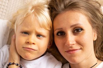 Portrait of mother and her little child baby boy hugging on bed at home. Child boy with strabismus eyes, squinting eyes, cross-eye. Motherhood, affection