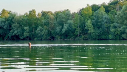 peaceful woman swimming in serene lake surrounded by dense green forest on a calm summer day