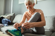 © Marko Geber - Senior woman tying running shoes before exercise at home