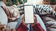 © Emin - Woman on sofa with blank screen smartphone in living room