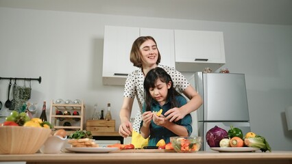 Wall Mural - Smart caucasian mother and asian girl cooking together and chopping vegetable or preparing salad for dinner. Happy mom and daughter making healthy food with fresh food. Healthy food concept. Pedagogy.