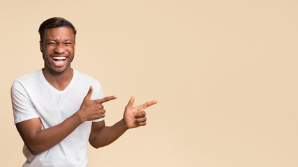 Poster - Funny Black Man Pointing Fingers Aside Laughing At Camera Standing On Yellow Studio Background. Panorama, Free Space For Text