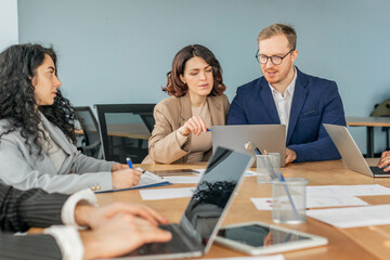 Aufkleber - A group of business professionals sit around a conference table in a modern office. They are engaged in a collaborative discussion, using laptops and tablets to work on a project