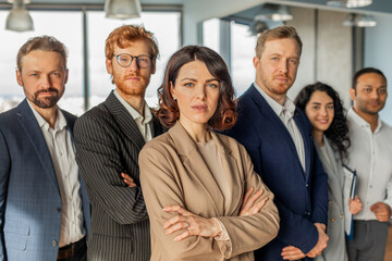 Aufkleber - A group of five diverse business professionals stand together in a modern office setting. The team is dressed in professional attire, with the woman in the center standing out in a brown blazer