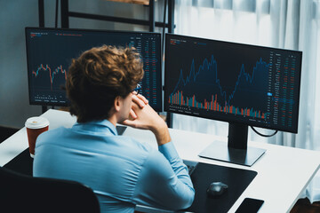 Wall Mural - Working young business trader focusing on market stock dynamic graph data in real time two pc screens with back side at modern office. Concept of analyzing dynamic financial exchange rate. Gusher.