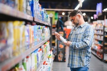 portrait of focused man buying household chemicals in supermarket, reading labels on bottles