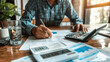 © NooPaew - Real estate investor reviewing loan documents and interest rates, with a calculator and financial reports on the table