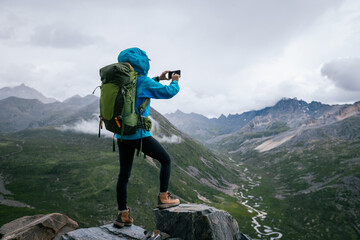 Wall Mural - Hiking woman taking photo with samrt phone on high altitude mountain top