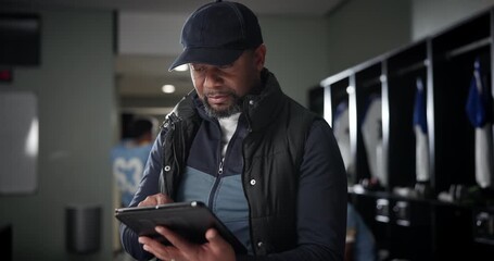 Sticker - Black man, football coach and tablet with team in locker room for strategy, game plan or sports news. African mentor, athlete or trainer scrolling or browsing on technology before match or playoffs