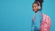 © Master old - Young african american girl teen student in denim clothes, backpack headphones isolated on blue wall background studio portrait. Education in high school university college concept. Mock up copy space
