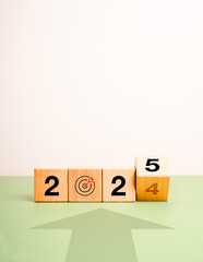 Poster - New goals new year 2025 concept banner. Arrow heading to target icon with flipping wooden cube blocks with 2024 change to 2025 calendar numbers on green and white background, vertical with copy space.