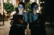 © qunica.com - Businesswoman focused on her tablet device at night, reflected on a glass window with illuminated city lights in the background.