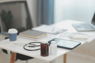 Doctor's working on laptop computer, writing prescription clipboard with record information paper folders on desk in hospital or clinic, Healthcare and medical concept. Focus on stethoscope