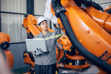 Wall Mural - Engineer woman working in advance machine factory. Indian female engineering staff work checking robot arm in assembly plant