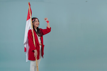 Excited Indonesian woman wearing a red jacket holding a flag while raising fist gesture.