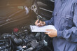 © KMPZZZ - Auto check, car service shop concept. Automobile repairman writing job checklist on clipboard, mechanic checking engine to estimate repair machine, inspecting maintenance by engineer at vehicle garage