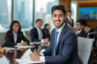 © Ricky - A young  man in business attire, sitting at the head of an elegant conference table with other professionals around him