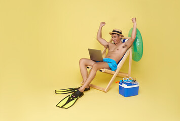 Wall Mural - tourist asian man working in laptop on deckchair isolated on yellow background. Summer vacation sea rest sun tan concept