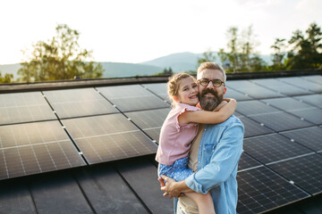 father with girl on roof with solar panels, hugging, looking at camera. rooftop solar or photovoltai