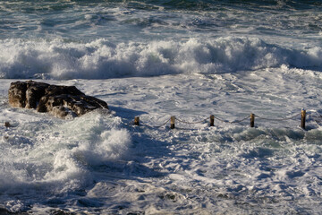 Wall Mural - Wild big waves smashing over barrier of ocean pool in storm