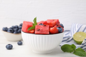 Wall Mural - Pieces of tasty watermelon, strawberries, blueberries and mint in bowl on white wooden table, closeup