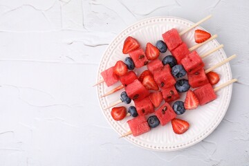 Poster - Skewers with tasty watermelon, strawberries and blueberries on white textured table, top view. Space for text