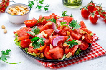 Wall Mural - Juicy salty sweet summer salad with watermelon, tomatoes, onion, peanuts and parsley on white background, top view