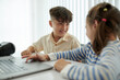 © DragonImages - Smiling children interacting with laptop while sitting at table in bright well-lit room with blinds in background
