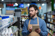 © Liubomir - Store employee using digital tablet to check inventory in supermarket aisle. Focused worker managing stock with technology in retail environment.