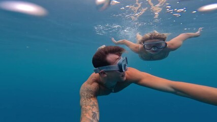 Wall Mural - Beautiful and cute couple of millennials young people snorkeling and diving together looking underwater for fishes and coral having fun and enjoying. Summer time swimming in the sea blue ocean.
