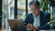 © ceren - Senior middle aged Asian businessman manager ceo using smartphone and laptop in office working online