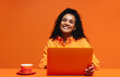 © Jacob Lund - Young woman smiling while working on a laptop in a vibrant monochromatic orange setting