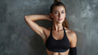 © VK Studio - A confident woman in a black sports bra strikes a pose with one arm behind her head, standing tall against a textured gray wall.