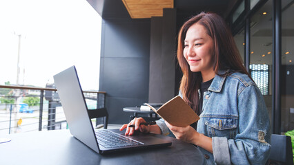 Wall Mural - Portrait image of a young woman writing on a notebook while working on laptop computer