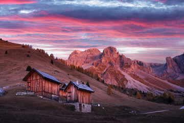 Wall Mural - wooden cabins, orange larches and mountains peaks in fuchiade valley in italian dolomites in autumn 
