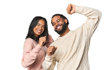 young latino couple in studio celebrating a special day, jumps and raise arms with energy.