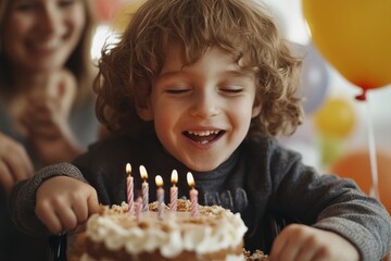 A cheerful child with curly hair smiling and reaching for a birthday cake with lit candles, surrounded by colorful balloons and people celebrating joyfully.