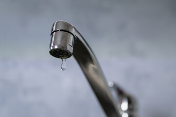 A drop of water drips from a leaky faucet. Close-up of a water dripping from a faucet